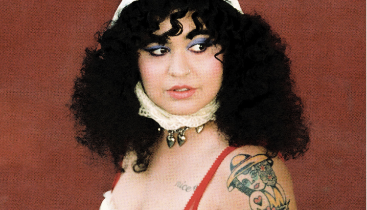 A woman poses looking to the right side against a burgundy red background while wearing a white outfit.